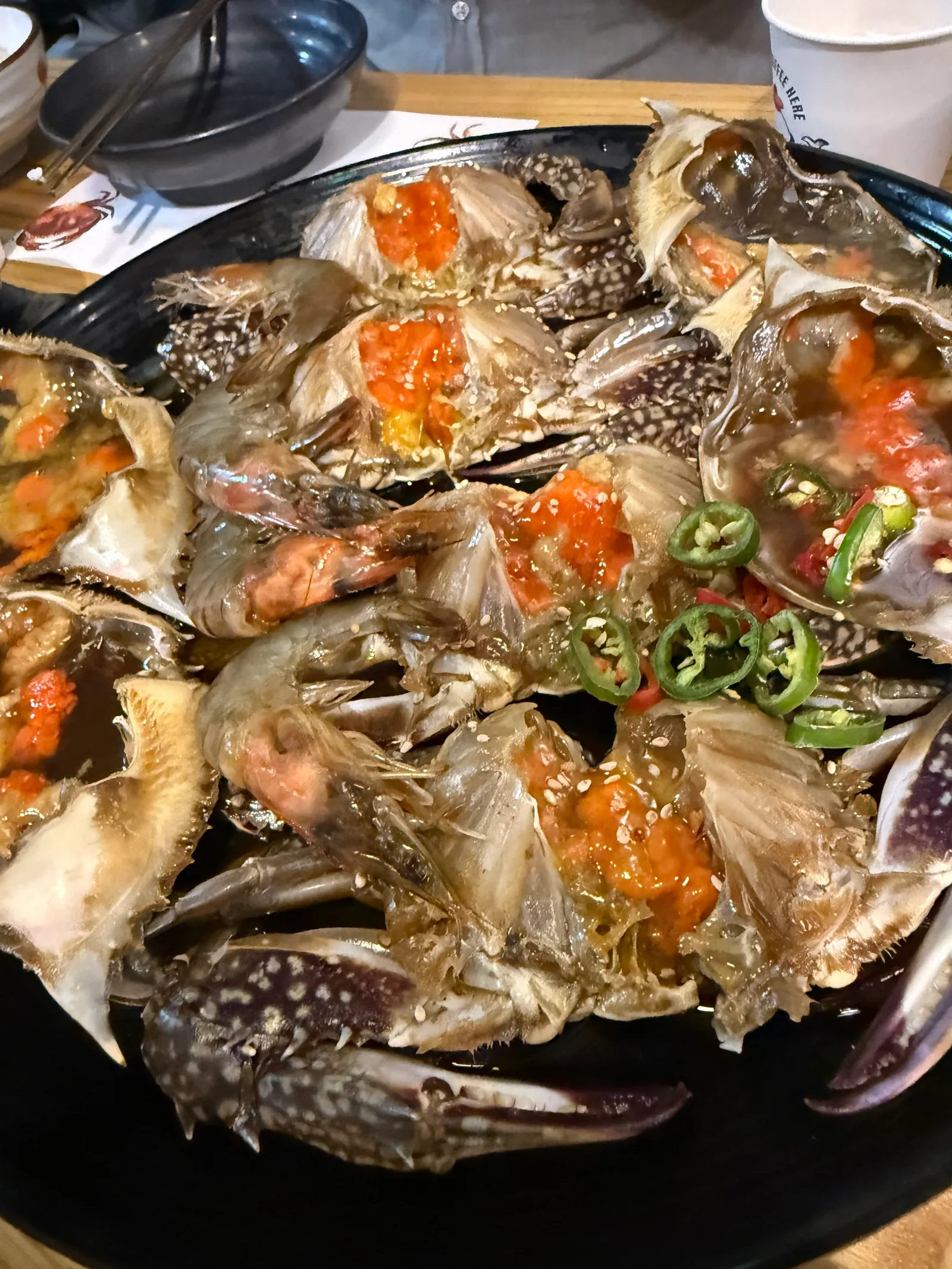 검은 접시에 담긴 알 밴 간장게장과 새우, 청양고추와 깨가 올라가 있다