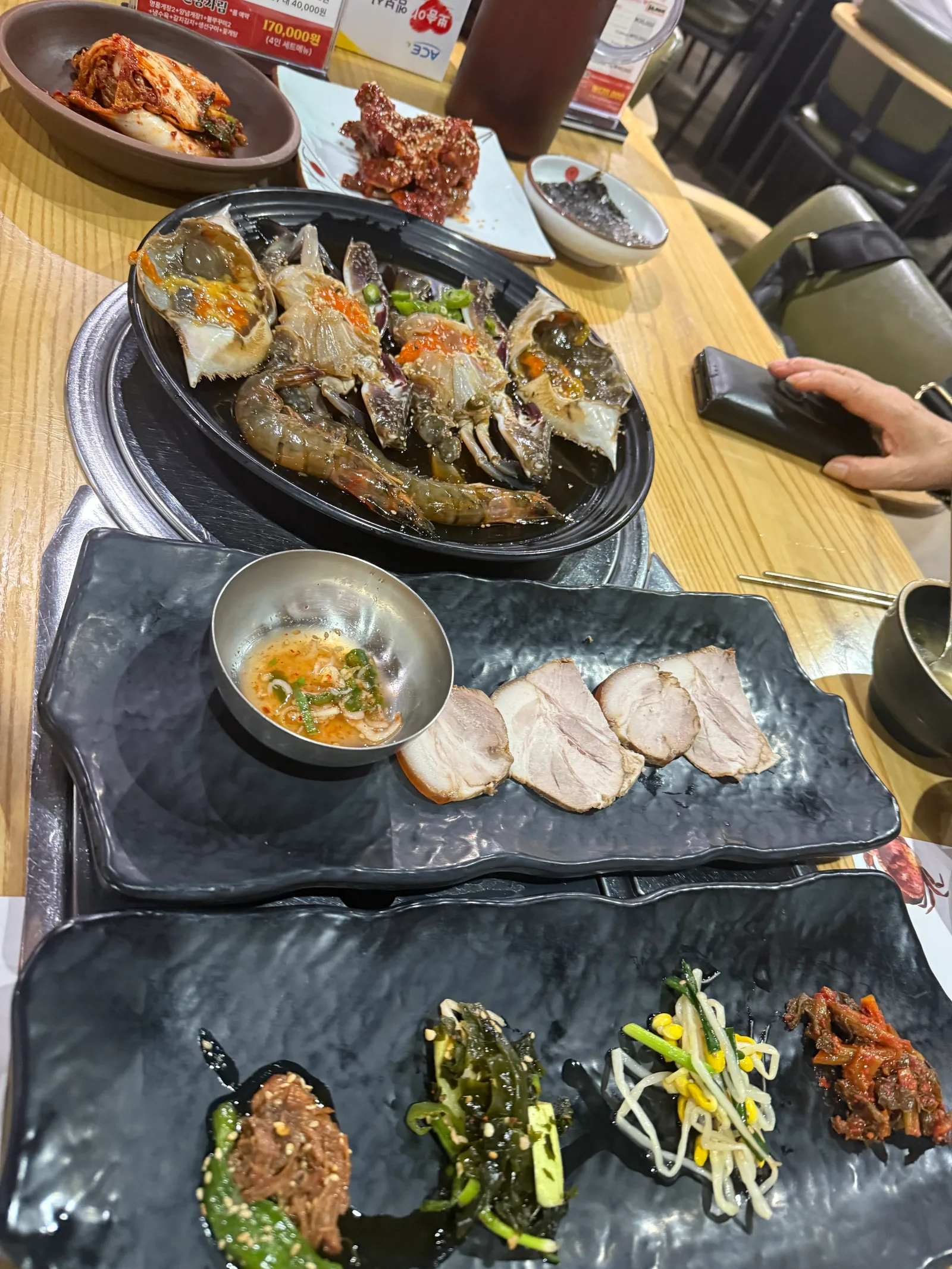 나무 테이블 위 수육과 양념장, 나물 반찬이 담긴 검은 접시들