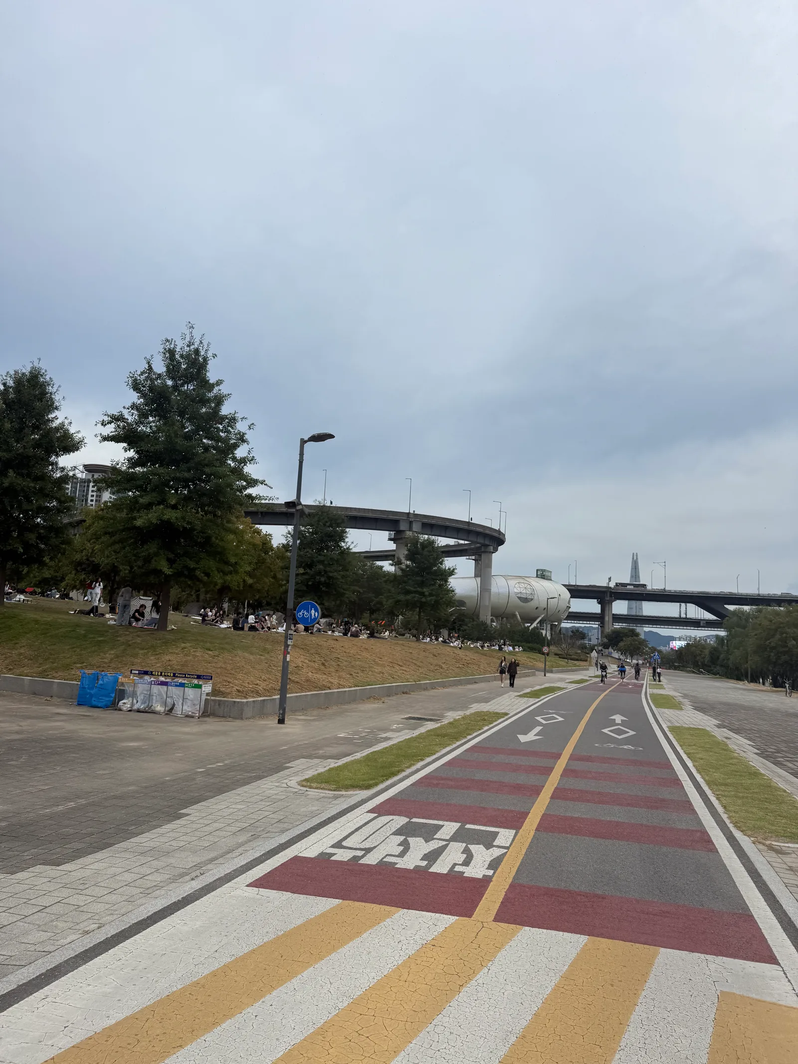 Han River park bike lane and pedestrian path with a recycling sign reading 재활용 분리배출 Please Recycle