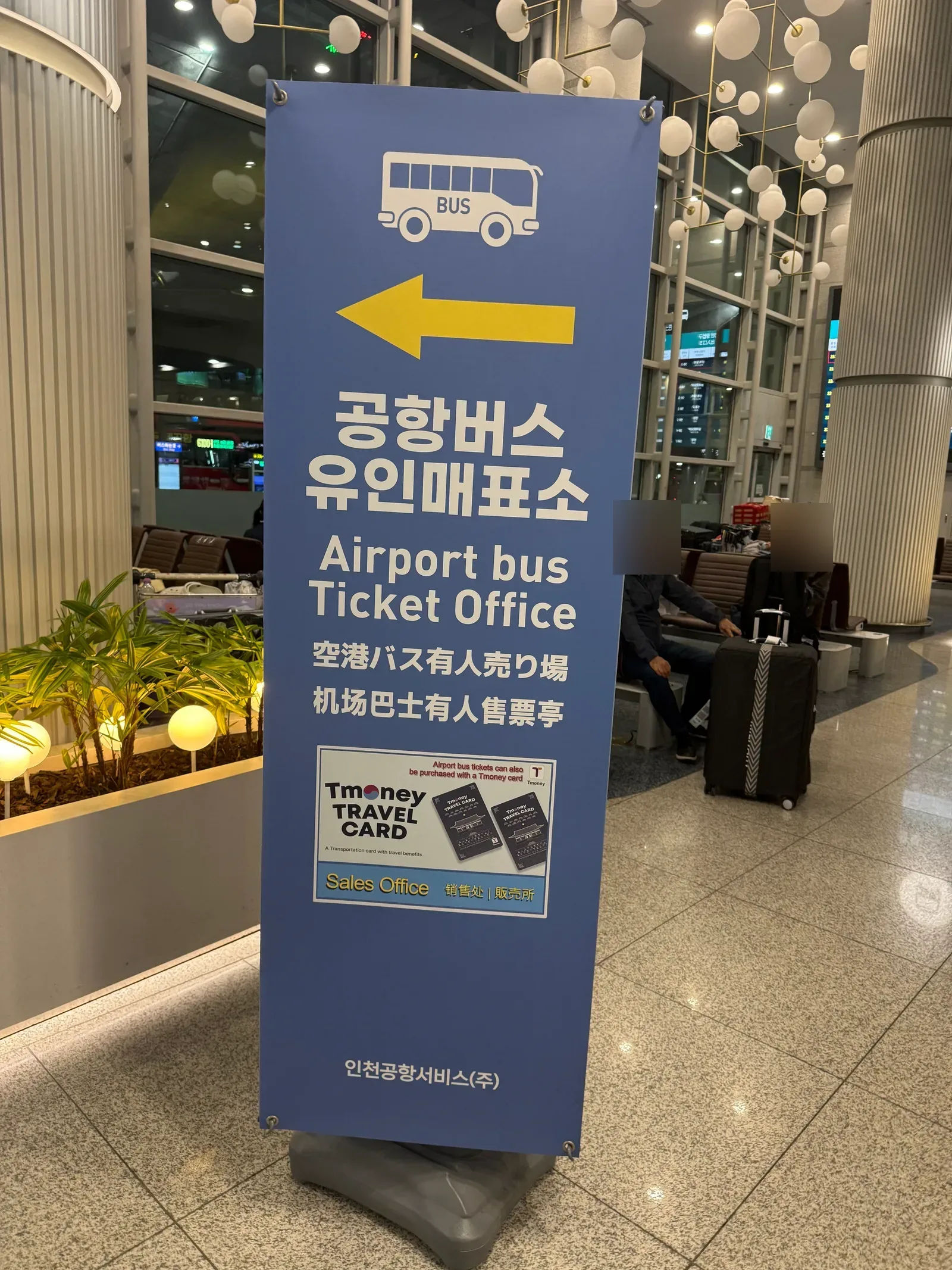 Standing banner for the Airport bus Ticket Office with an arrow, noting that tickets can also be bought with a Tmoney card