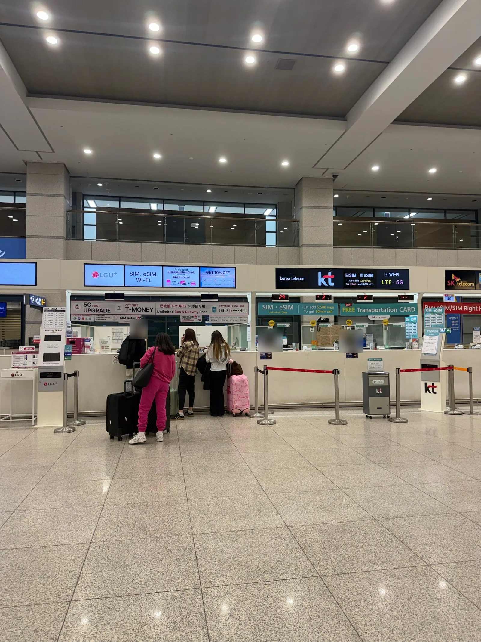Carrier counters standing side by side on an airport arrival floor, with LG U+, KT and SK telecom signs above them